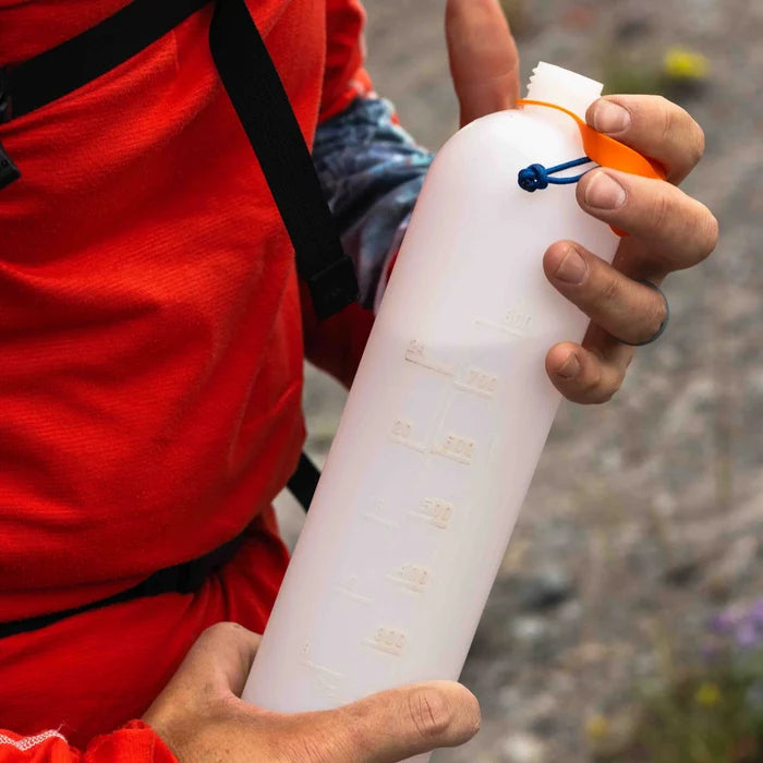 Thru Bottle open and with an orange lid being held by a person in a red shirt on a trail.