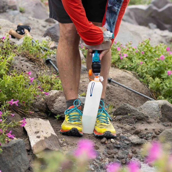 Thru bottle being held between two feet while a cnoc water bladder with a sawyer water filter attached is being squeezed to filter water into the bottle