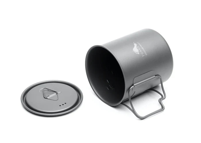 Toaks 450ml Cup on its side with the handle open and the lid laying next to it on a white background