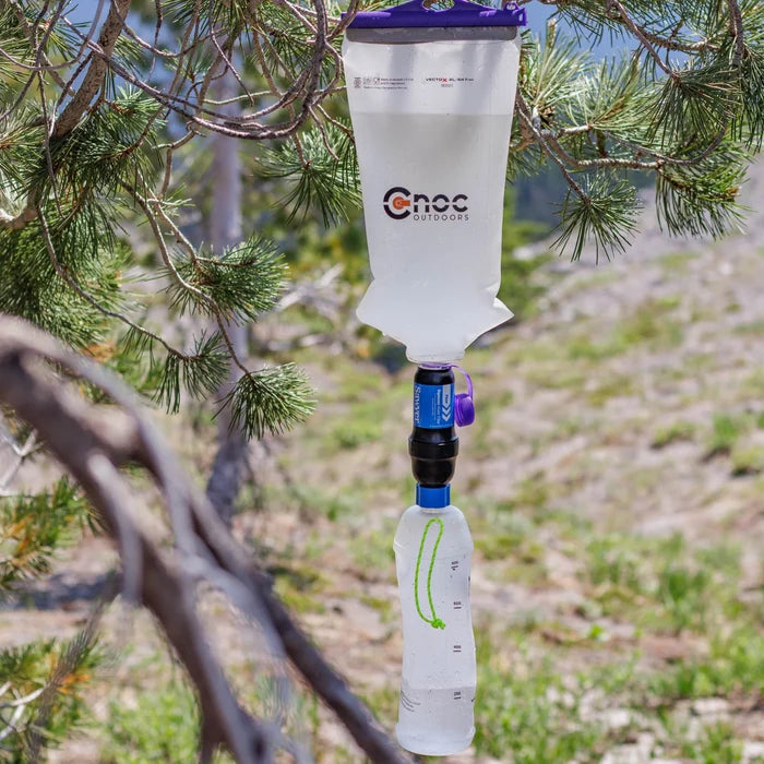 Cnoc Vecto X with purple lid open and hanging from a tree attached to a sawyer filter with a Green Vessica bottle attached at the bottom to create a gravity filter