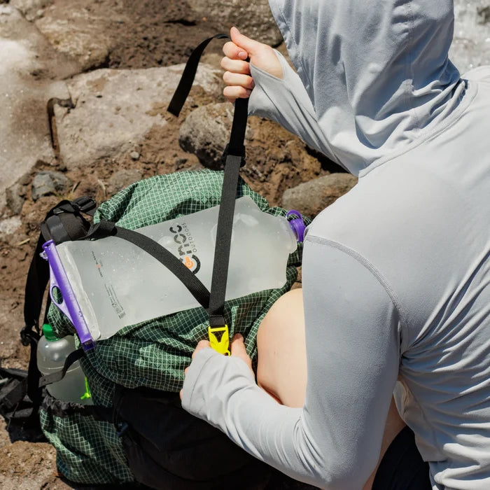 Cnoc Vecto X purple lid full of water being strapped to the top of a backpack